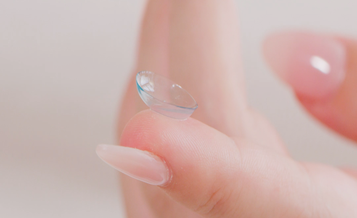 Close-up of a translucent contact lens perched on the tip of a finger.