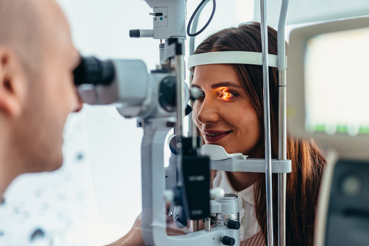 Woman undergoing a slit-lamp eye exam, looking into the device while a clinician peers through the microscope from the left.