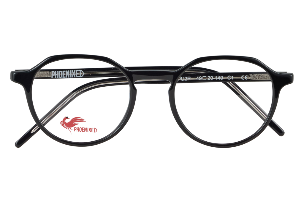 Black round eyeglasses with a glossy frame resting on a clear glass block; Phoenixed logo visible on the left lens and branding along the temple.