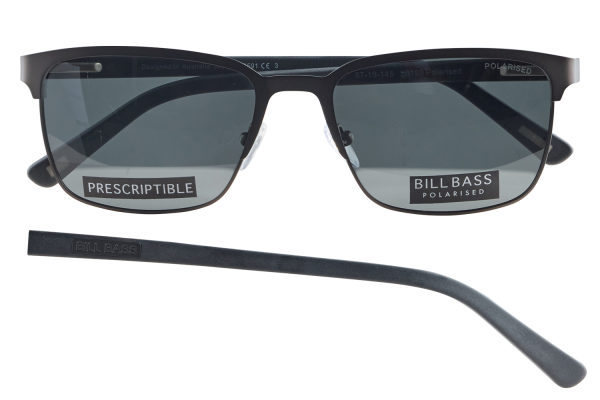 Pair of black rectangular sunglasses with dark lenses, labeled BILL BASS POLARISED and PRESCRIPTIBLE on the lenses, plus a separate black temple piece lying nearby.
