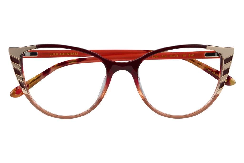 Red-framed glasses with gold accents on the temples, resting on a clear stand for display purposes (LULU GUINNESS branding visible).