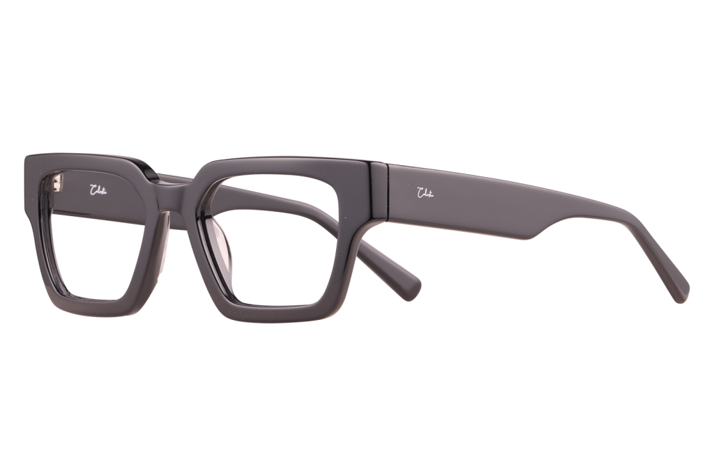Pair of thick, rectangular black eyeglasses resting on a light surface, seen from the side with one temple extended outward.