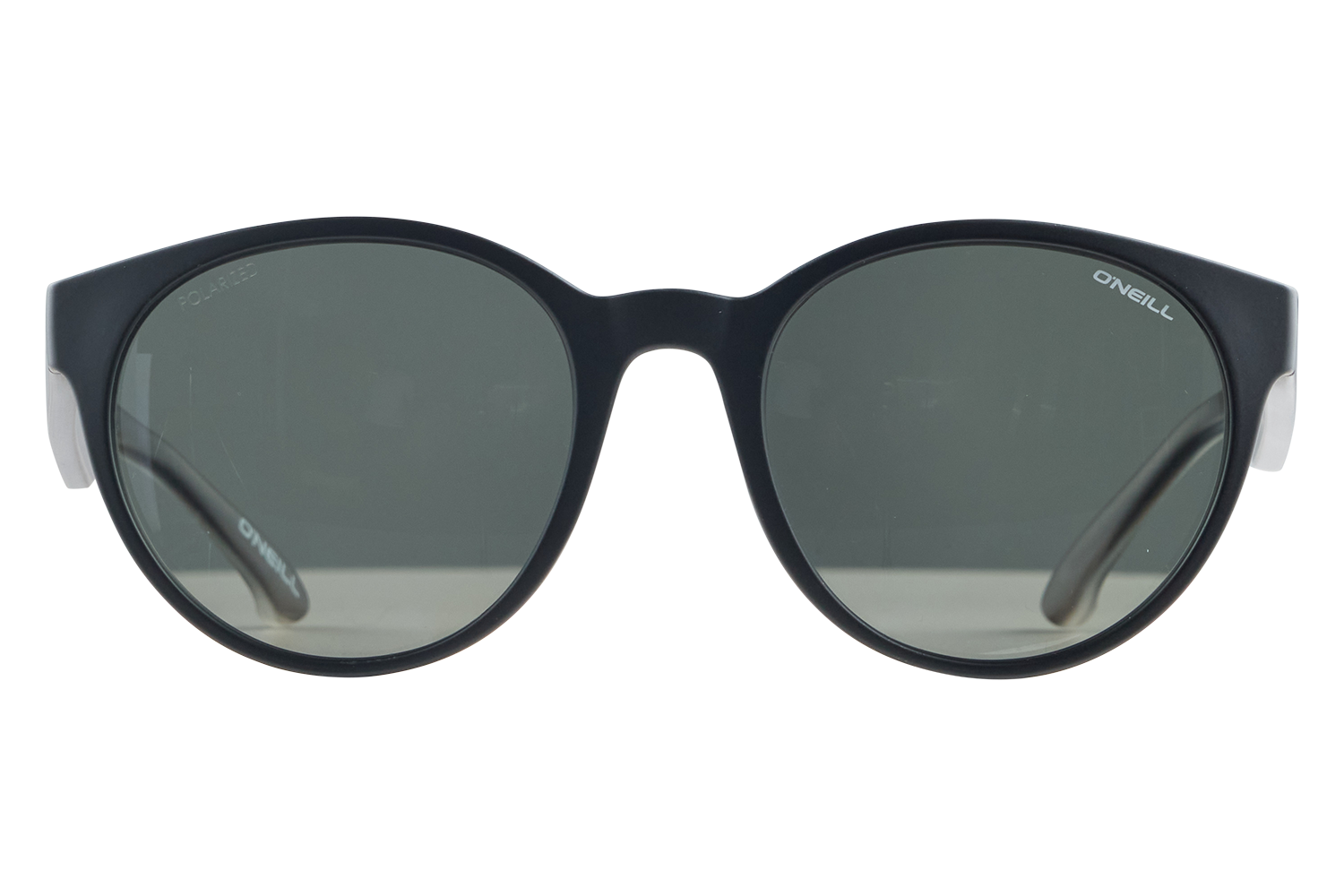 Black rounded sunglasses with dark grey lenses resting on a white surface; O'Neill branding on the temples.