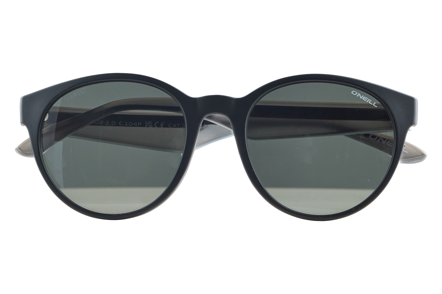 Black round-frame sunglasses with dark green lenses displayed on a small clear stand; brand 'O'Neill' visible on the right temple side.